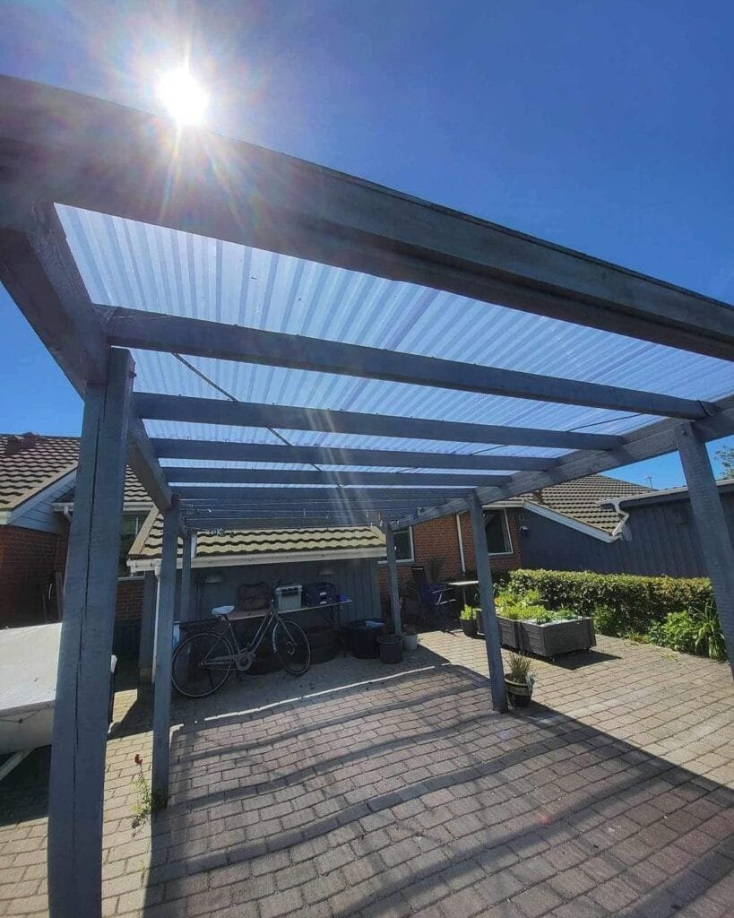 Træpergola med solbeskinnet tag og cykel under.
